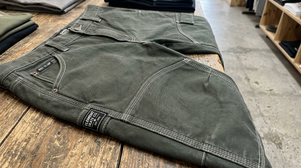 Affordable durable skate pants displayed flat on a concrete urban background.