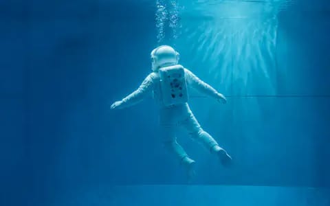 A spacesuited astronaut floating underwater in a pool, mimicking the weightless conditions the body experiences in orbit